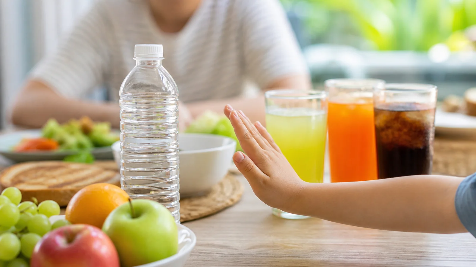 Child's hand moving sugary drinks aside in favour of water and fruit